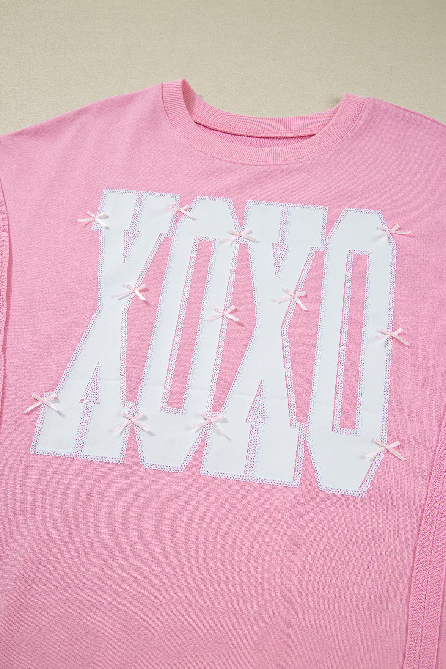 Pink sequin bow XOXO graphic baggy sweatshirt blouse by Lavendar Lane Clothing, featuring exposed seams and playful design.